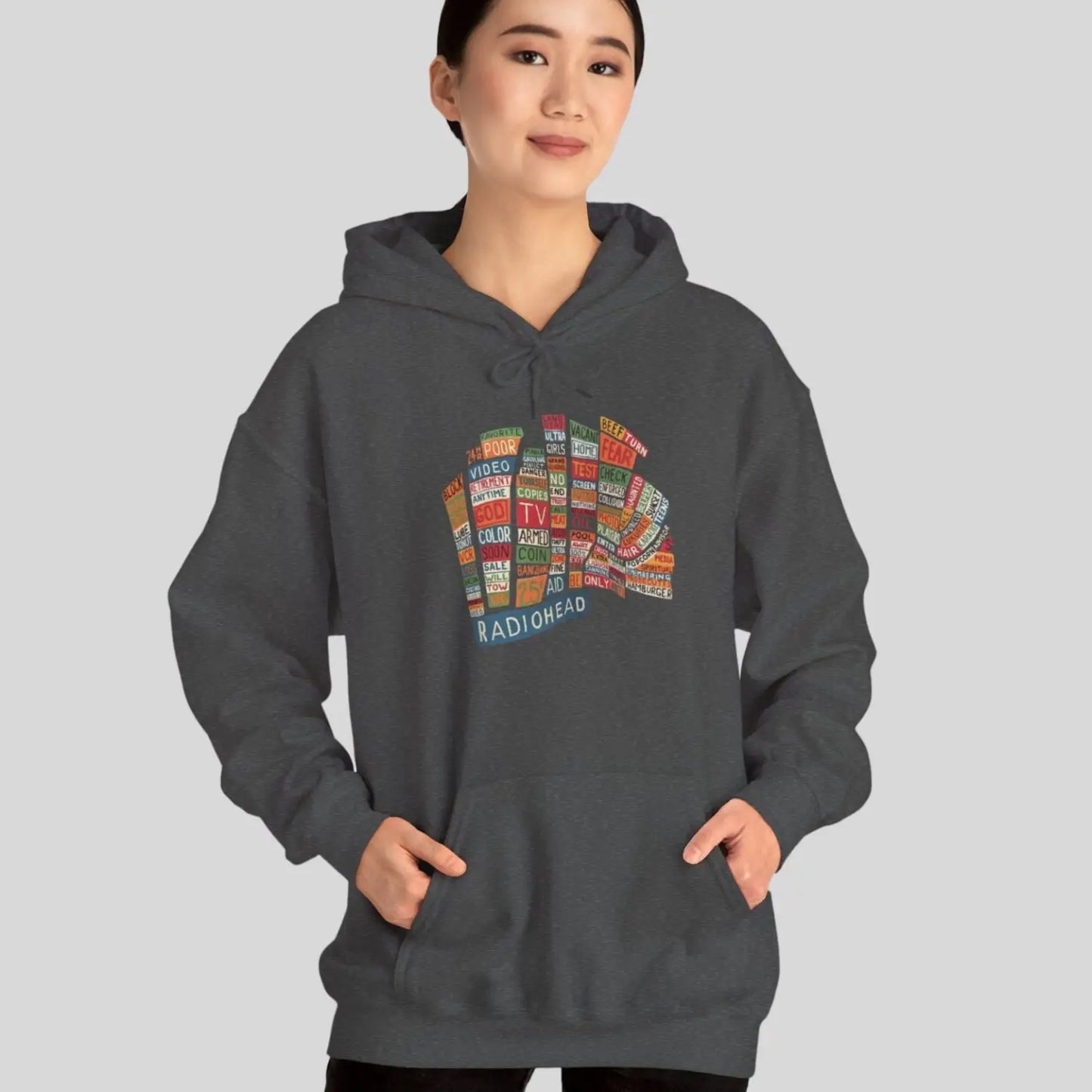 Adult woman wearing dark heather grey hoodie of Radiohead Hail to the Thief album featuring a bear-shaped block of colorful words and a RADIOHEAD label beneath.