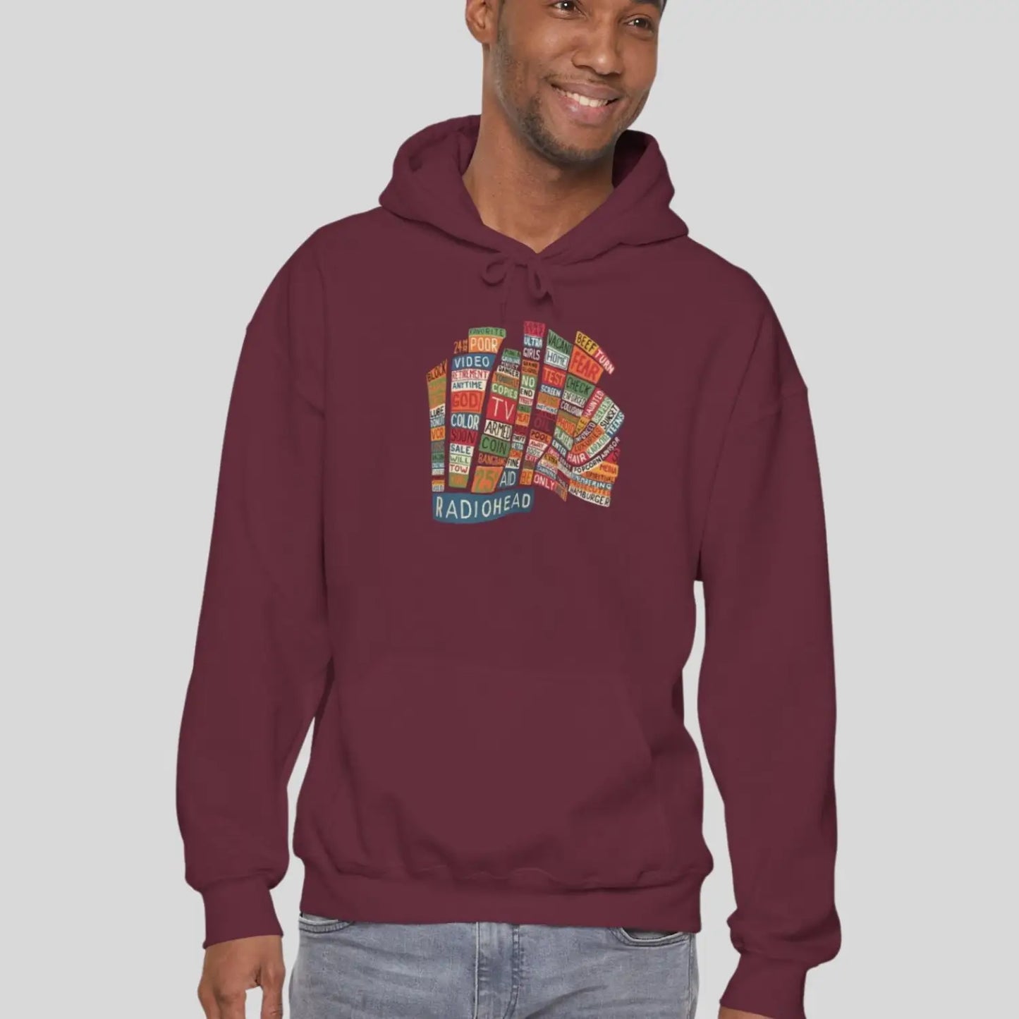 Adult man wearing maroon red hoodie of Radiohead Hail to the Thief album featuring a bear-shaped block of colorful words and a RADIOHEAD label beneath.