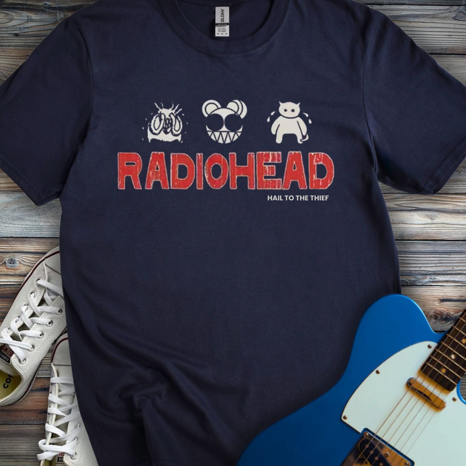 Navy blue color of Radiohead graphic t-shirt featuring red distressed band logo with iconic bear and cartoon artwork from Hail to the Thief album, stylish music band tee for alternative rock fans.