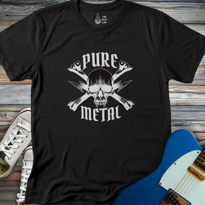 The Pure Metal T-shirt features a black base with a white skull and crossed bones graphic and "PURE METAL" in bold, gothic font. Displayed on a wooden surface beside white sneakers and a blue electric guitar.