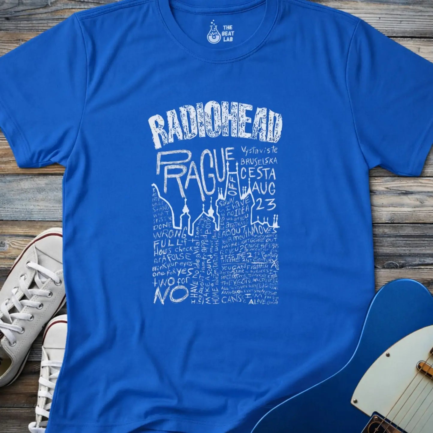 Royal blue color adult unisex t-shirt gildan 64000 Radiohead Prague concert graphic t-shirt with distressed RADIOHEAD header, large hand-drawn PRAGUE text, date details, and dense handwritten lyric-style lettering.