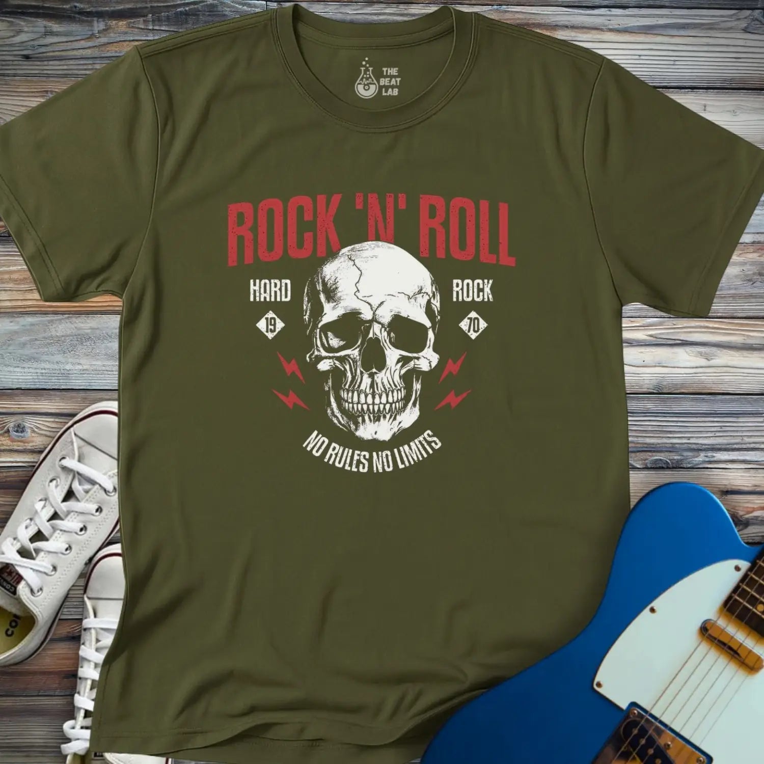 The Rock 'N' Roll 1970 T-shirt features a skull graphic with red lightning bolts and text reading ROCK N ROLL, HARD ROCK, 1976, and NO RULES NO LIMITS. Displayed on wood beside white sneakers and a blue electric guitar.