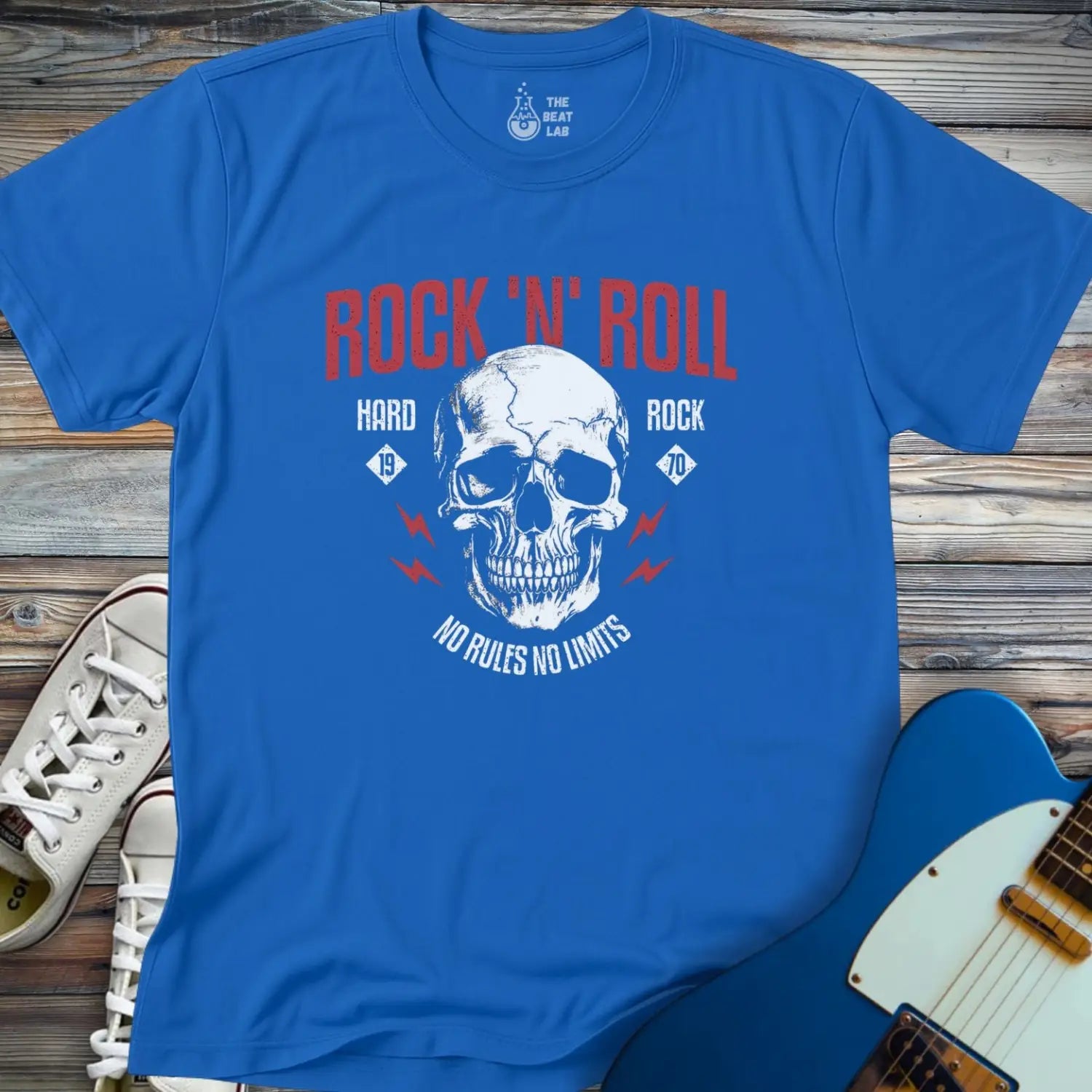 The Rock 'N' Roll 1970 T-shirt features a blue design with a skull graphic, red ROCK N ROLL text, blue lightning bolts, and the phrases Hard Rock 1970 and No Rules No Limits, shown on a wooden surface with sneakers and a blue guitar.